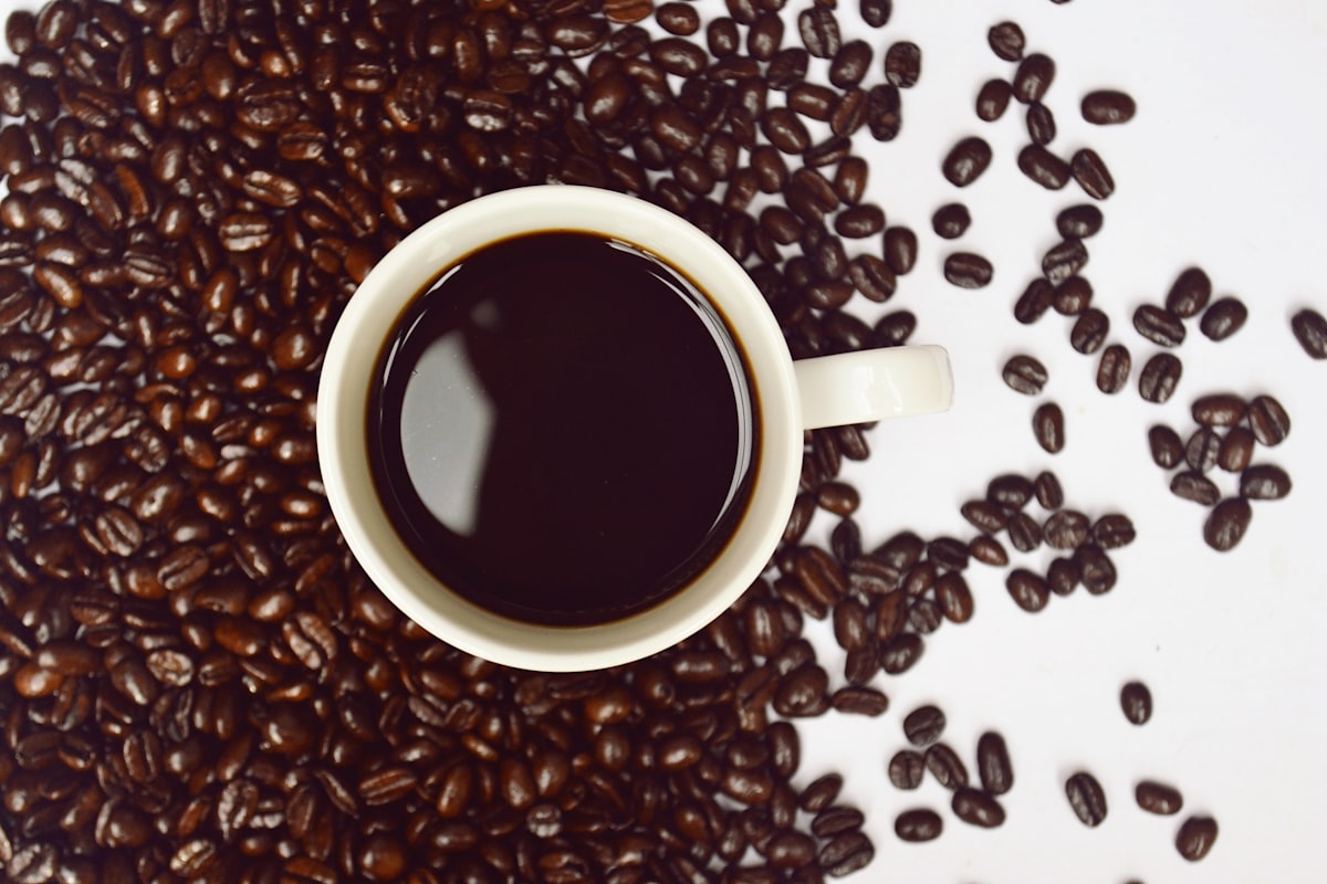 コーヒー豆に囲まれた、コーヒーが注がれた白いカップ